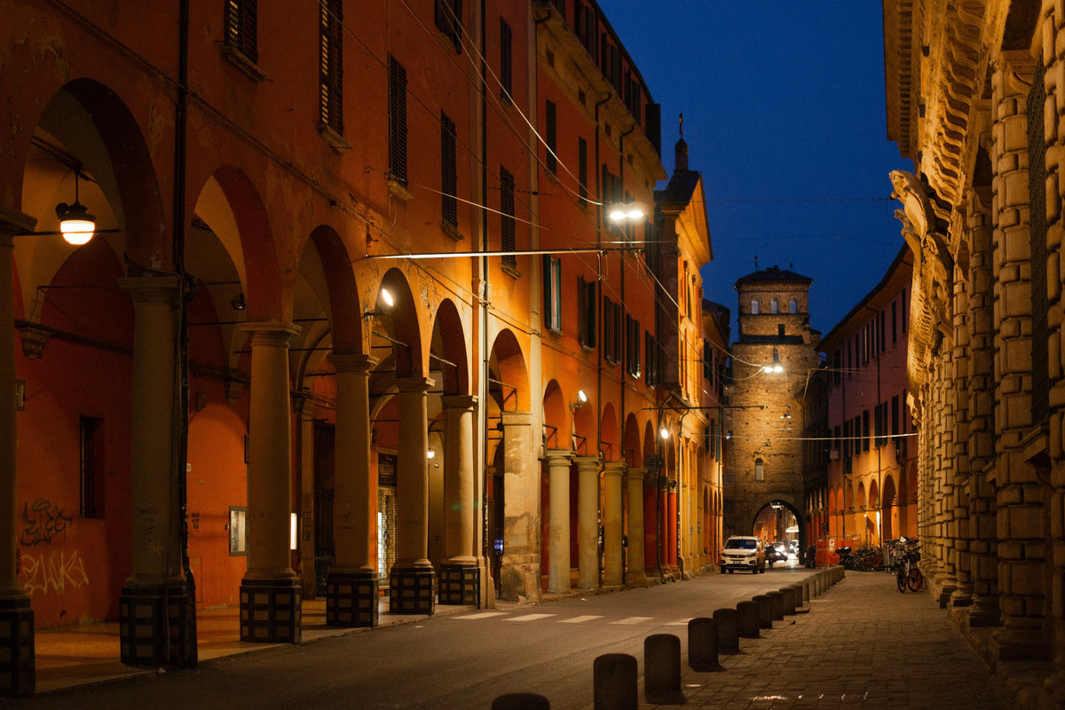 A lit portico in Bologna at dusk, with arches and columns lining the pavement