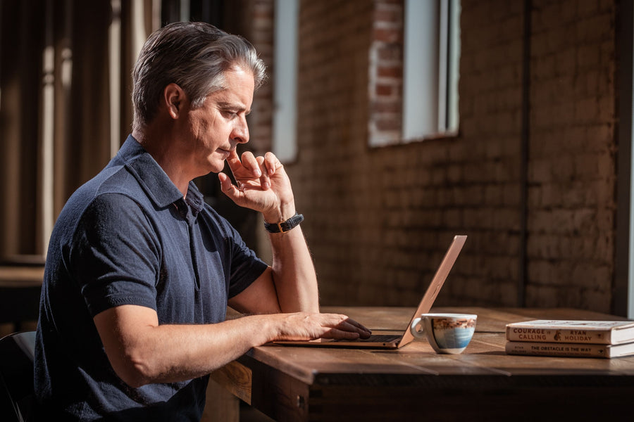 A person working on a laptop in a sunlit brick-walled room in Venice, with a coffee nearby