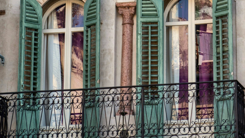 Green wooden shutters and a wrought-iron balcony on an old apartment building in Verona, Italy