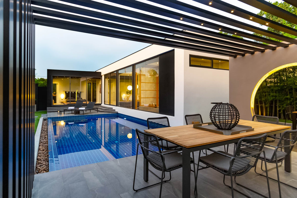 Pergola, outdoor dining table and pool at a Villoft pool villa at dusk