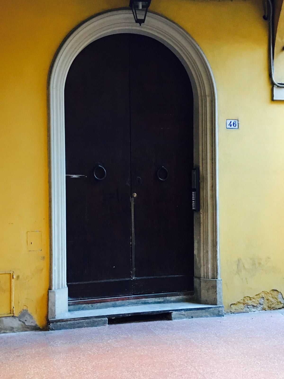 An arched wooden door in a yellow Bologna wall