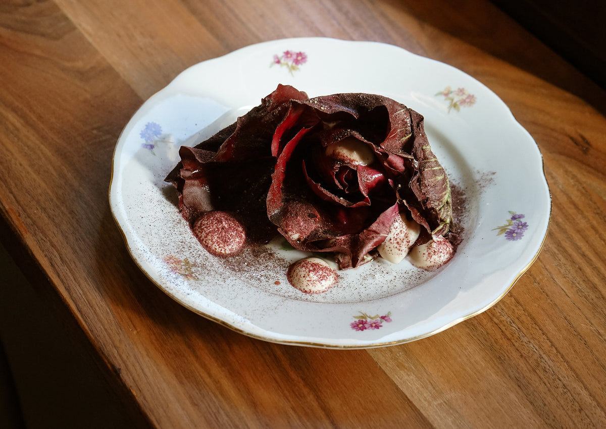 A dish topped with red radicchio leaves on a floral porcelain plate at Ahimè