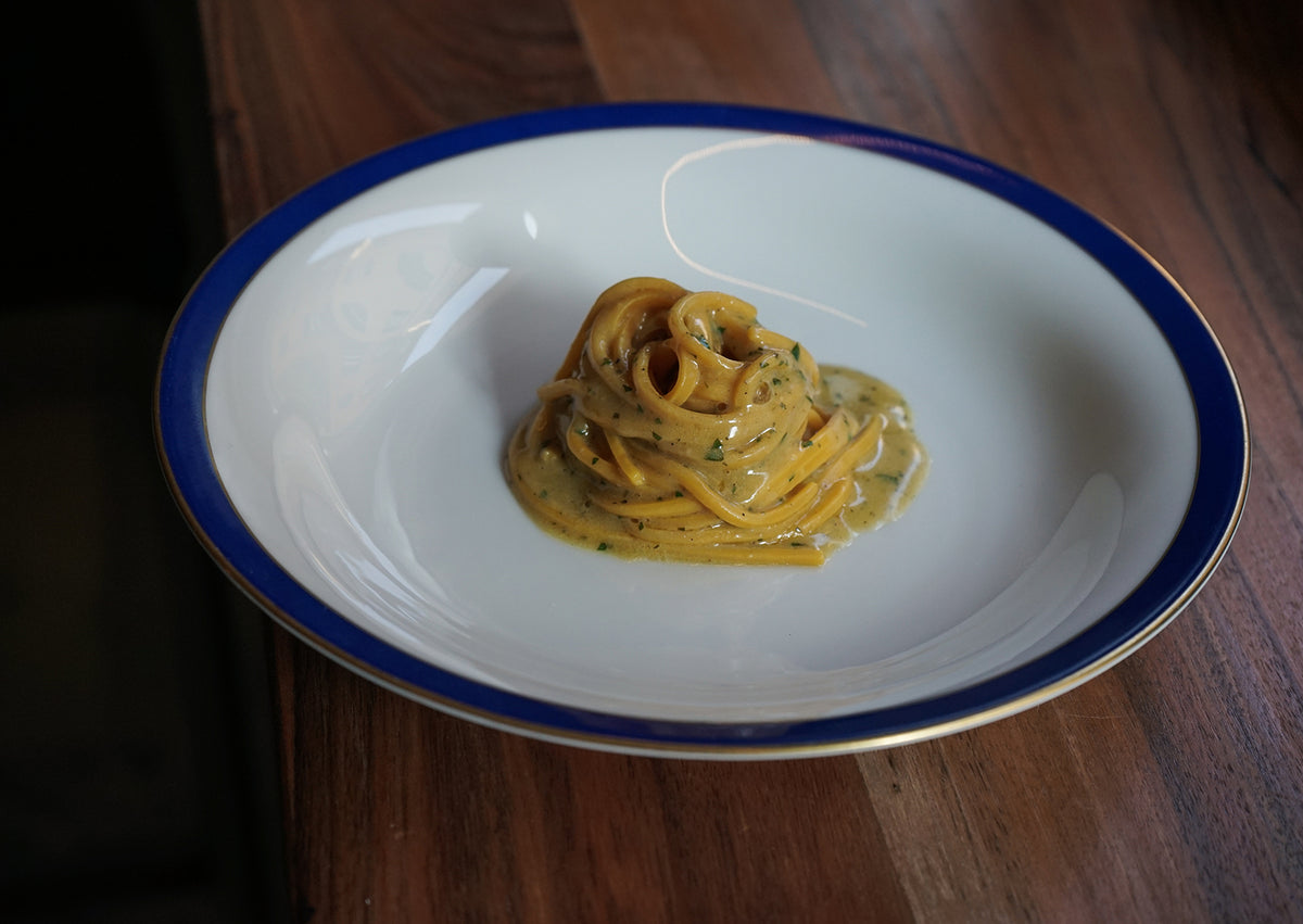 A nest of spaghetti in a creamy sauce on a blue-rimmed plate at Ahimè