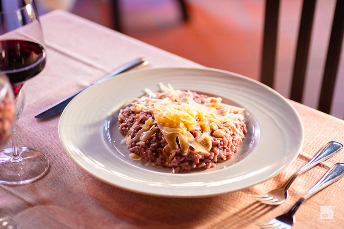 A plate of red risotto topped with cheese shavings, with a glass of red wine at Al Sangiovese