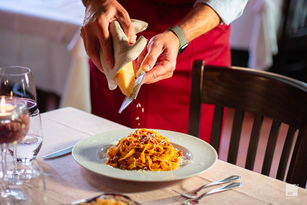 Cheese being grated over a plate of tagliatelle with meat sauce at Al Sangiovese