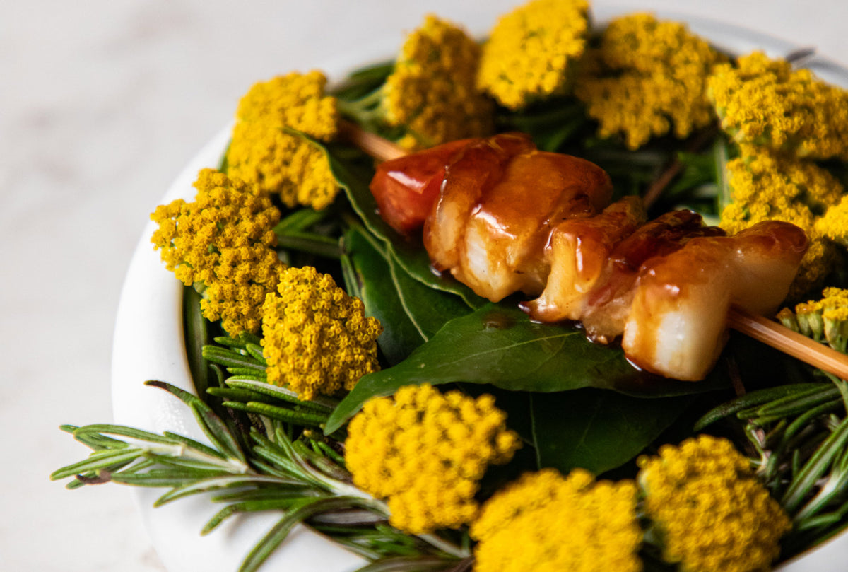 A glazed skewer on leaves and yellow flowers at I Portici