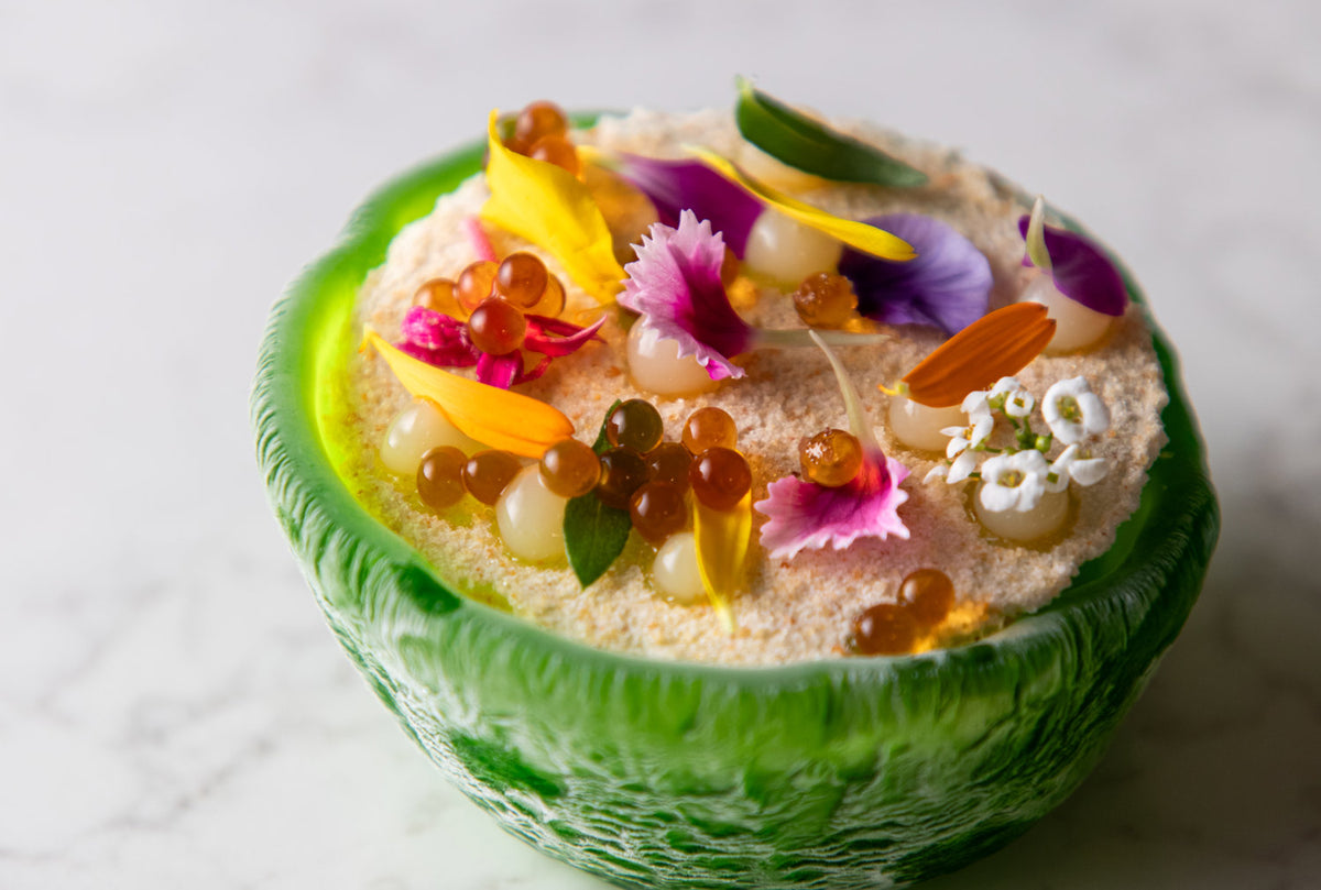 A green glass bowl topped with edible flowers at I Portici