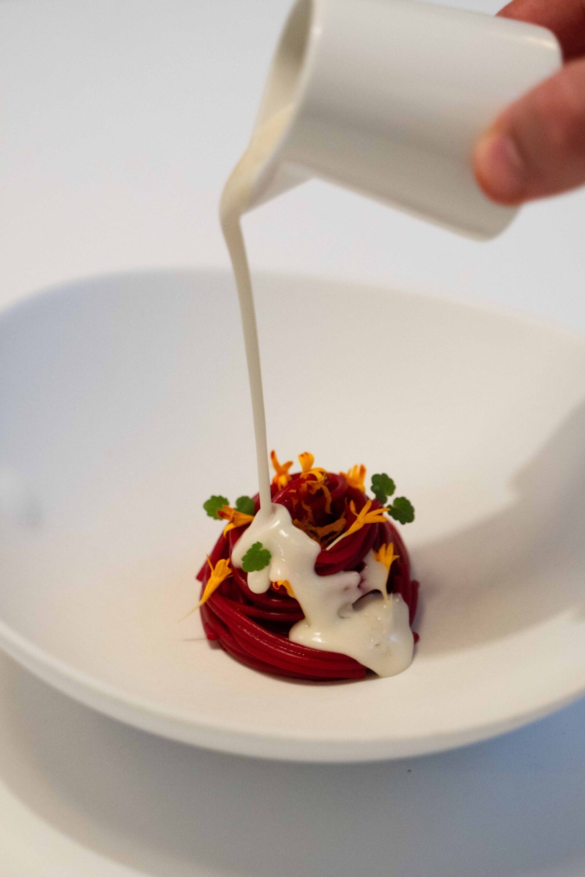 Cream being poured over a red dish garnished with petals at La Porta