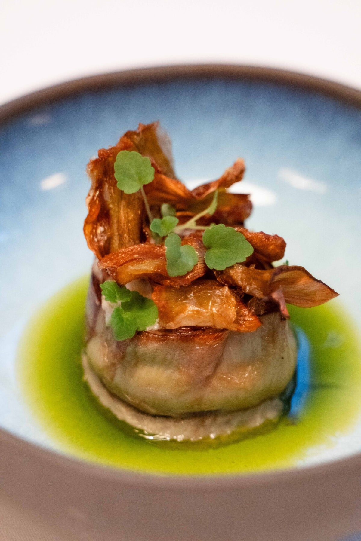 A dish topped with crisp vegetables and herbs in green oil at La Porta
