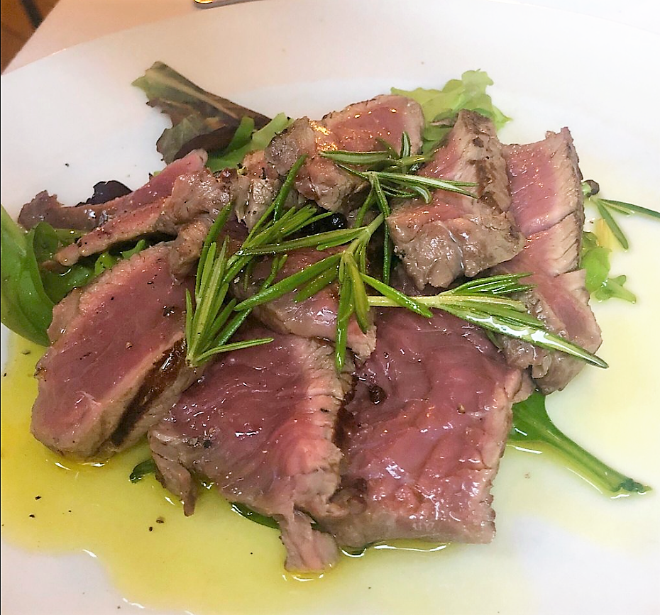 Sliced steak with rosemary and olive oil on salad leaves at Posta
