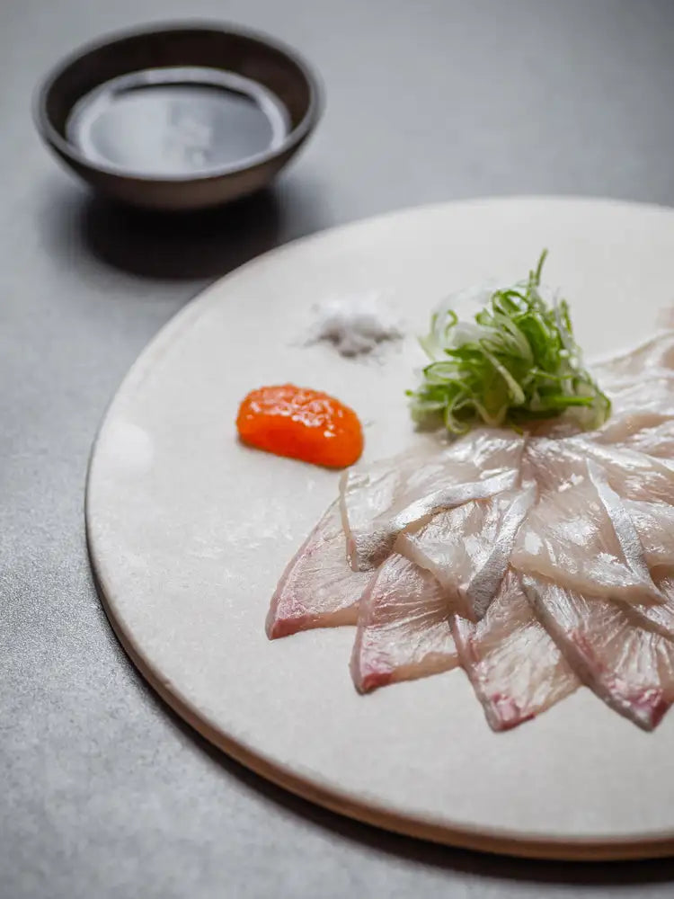 Thinly sliced raw fish with spring onion and a small sauce bowl at Seta