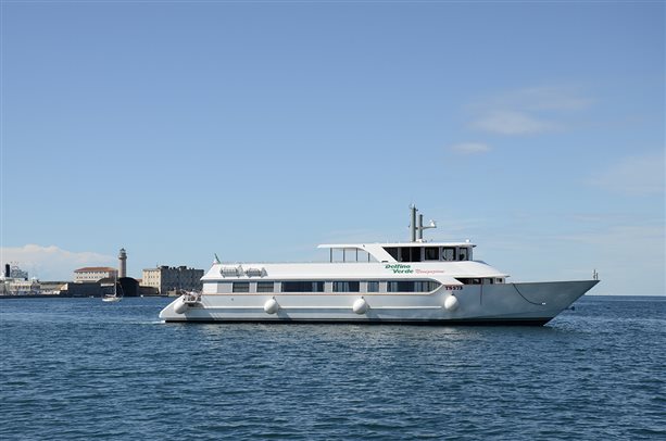 The Delfino Verde boat at sea with the Lanterna lighthouse behind