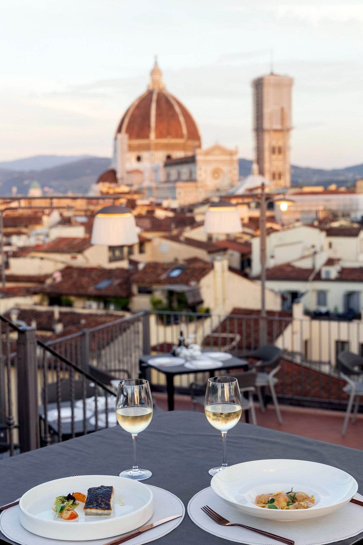 Plated dishes and white wine on the terrace of B-Roof Restaurant, Duomo behind