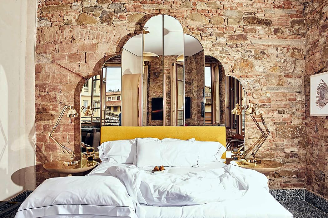Double room with exposed stone wall and arched mirror at Hotel Calimala