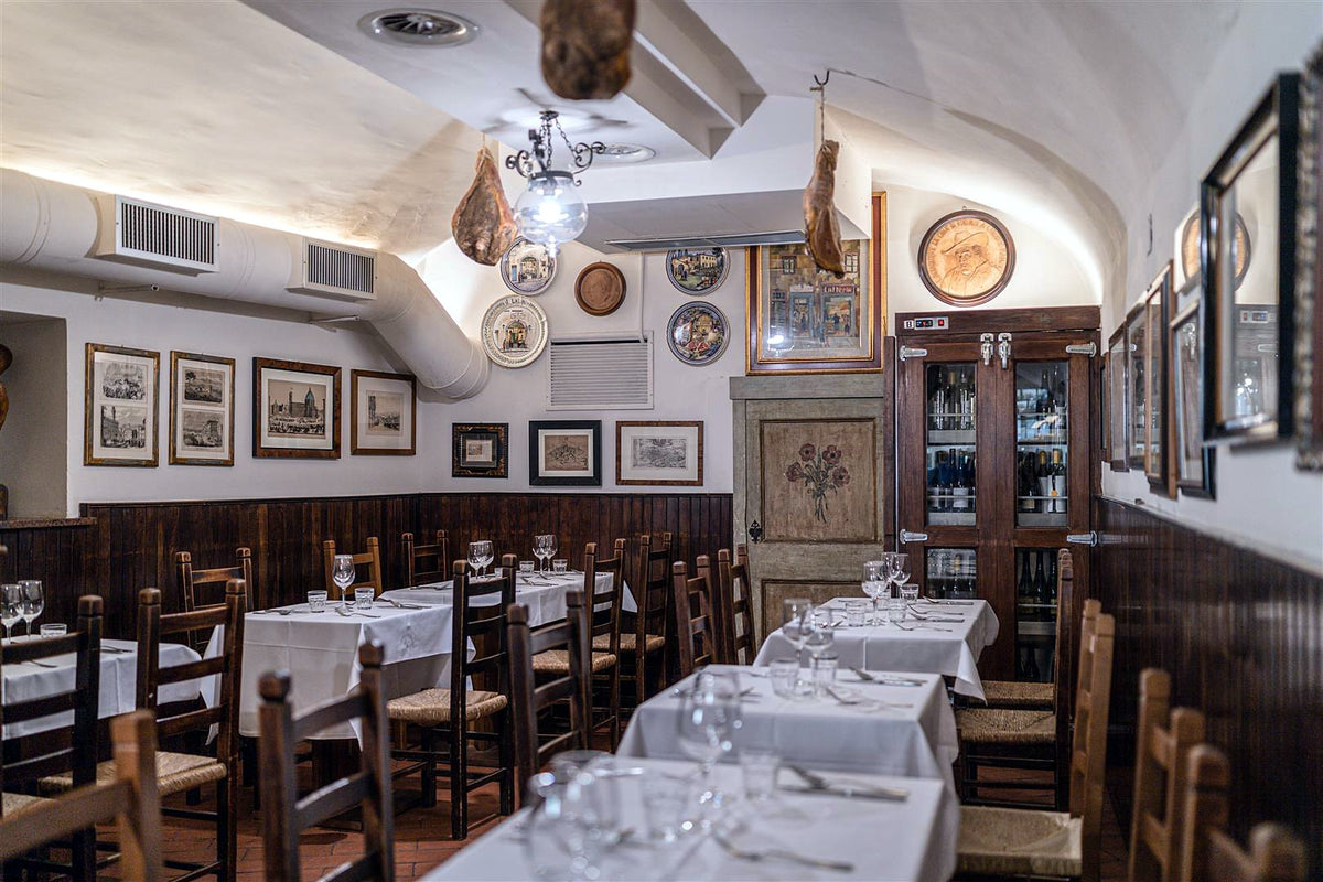 Dining room with hanging hams and laid tables at Il Latini