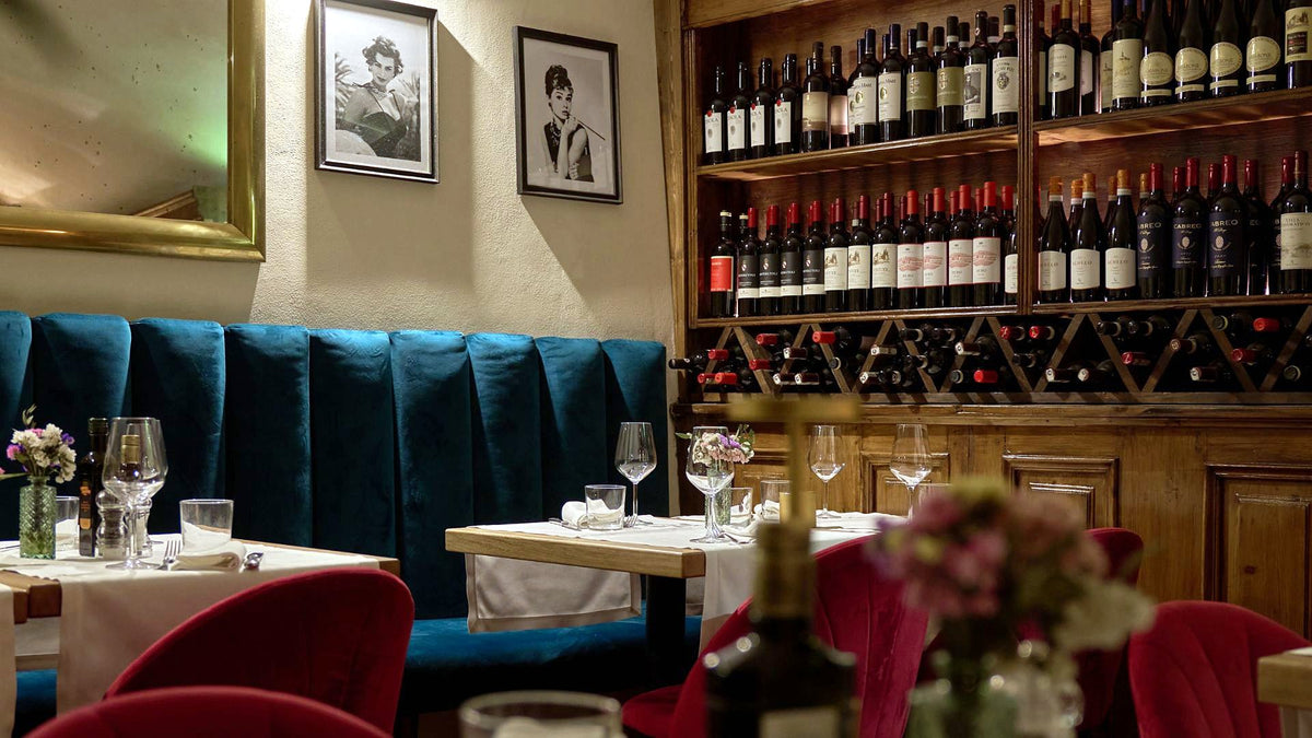 Dining room with velvet banquette and wine wall at Osteria Belle Donne