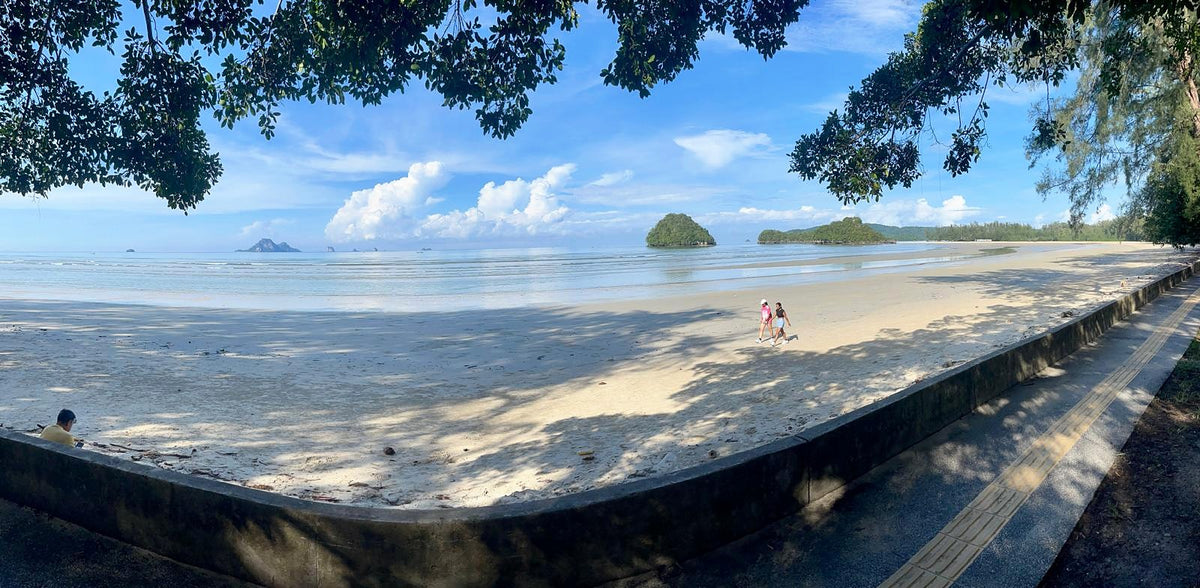 A wide, tree-shaded beach and seafront promenade on the Andaman coast near Ao Nang