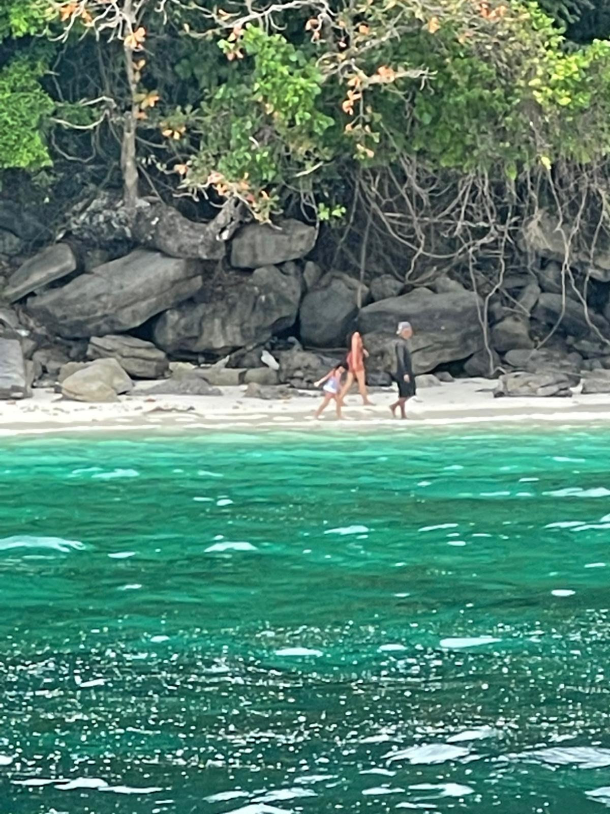 Beachgoers on a small sandy cove below a rocky, wooded shore on the Andaman coast