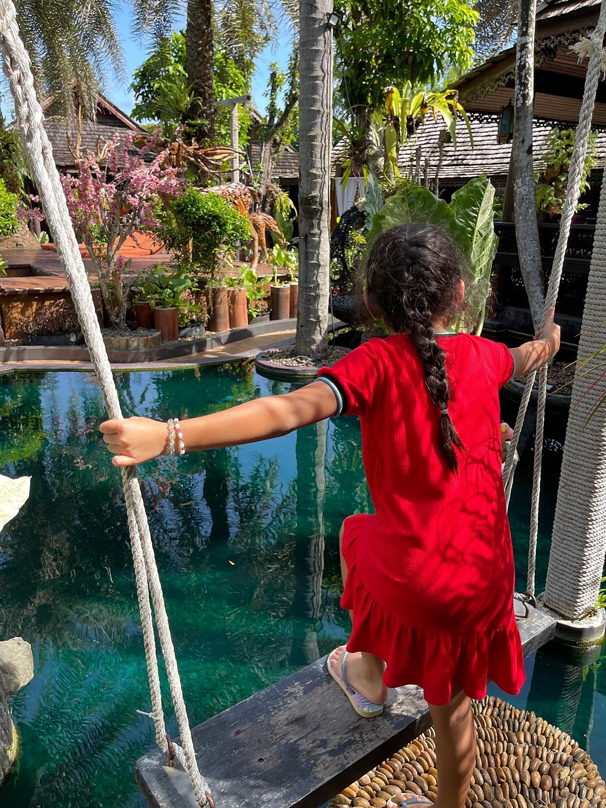 A child on a rope-hung wooden plank over a garden pond in Krabi
