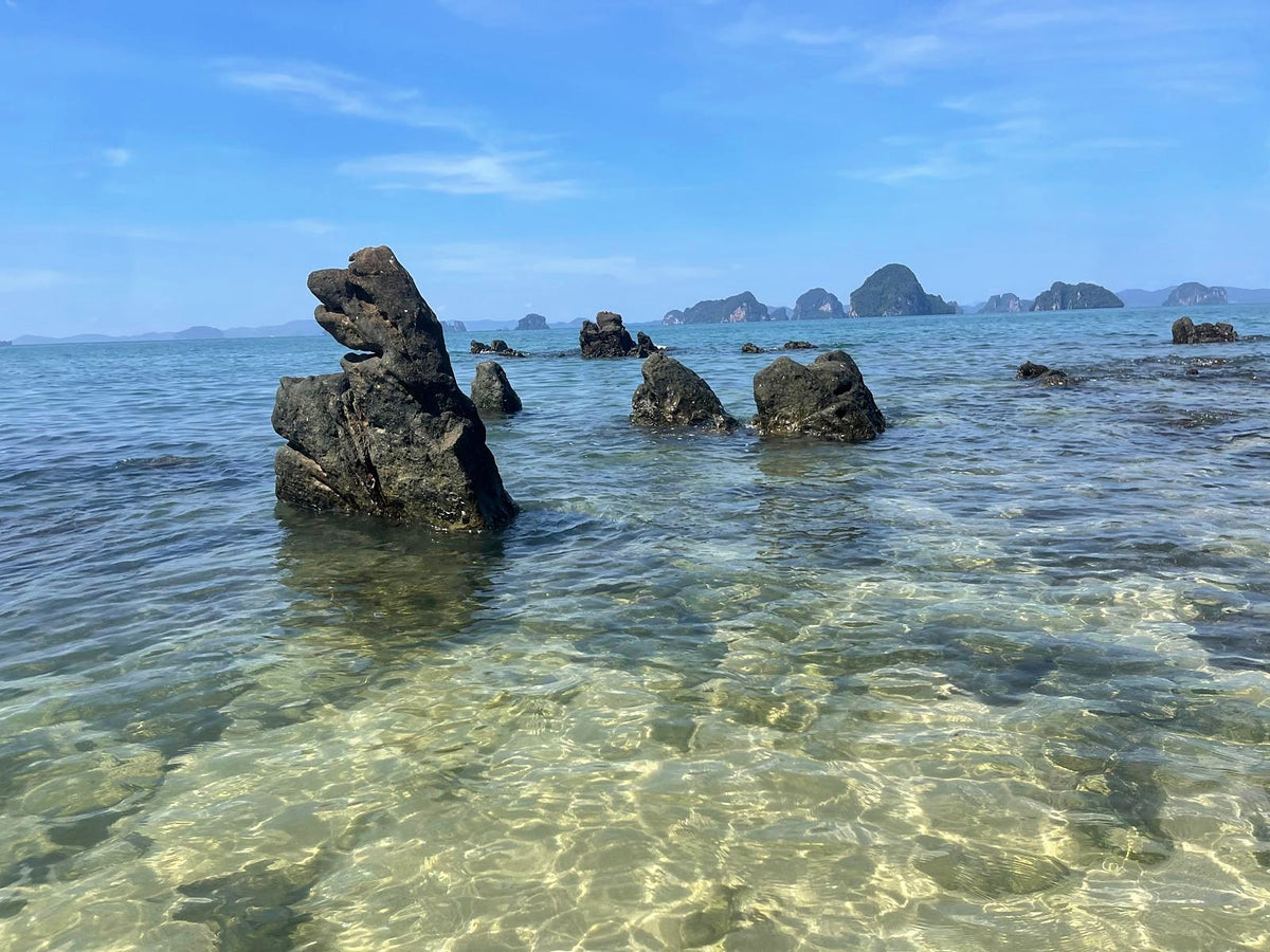 Dark rocks in clear shallow water, with limestone islands in the distance, Andaman coast
