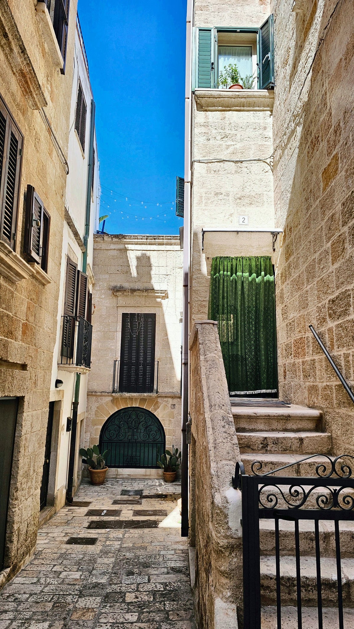Stone steps and a green gate in a sunlit alley