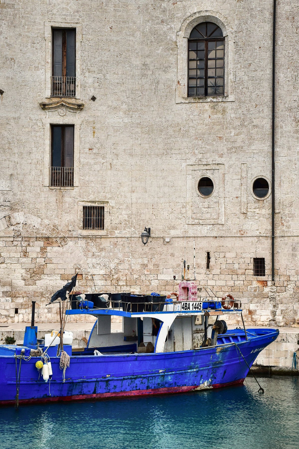 A blue fishing boat moored against the old stone walls
