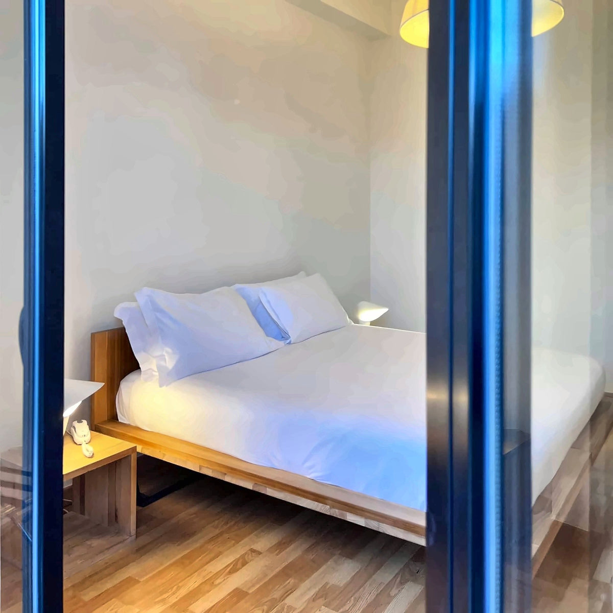 A minimalist double room at Imago+ framed by a blue doorway