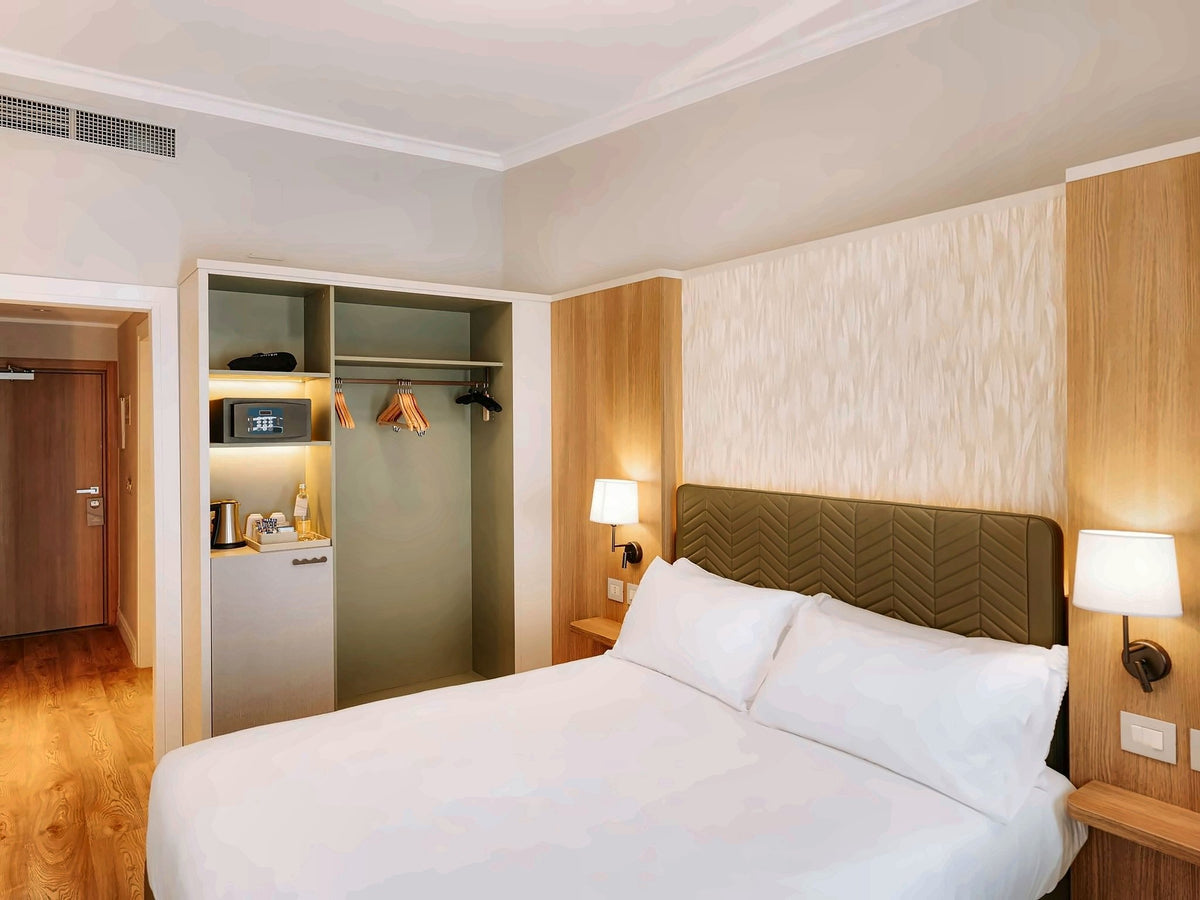 Guest room at Mövenpick Hotel Bari with a green headboard and warm wood finishes