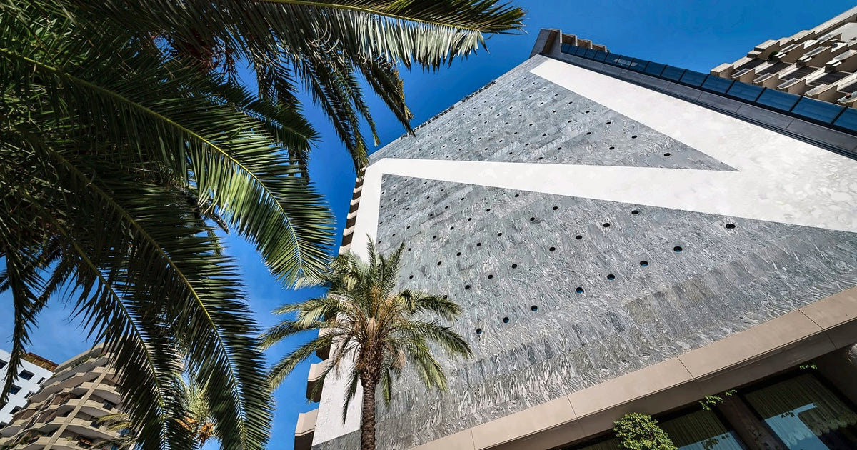 The facade of The Nicolaus Hotel rising behind palm trees