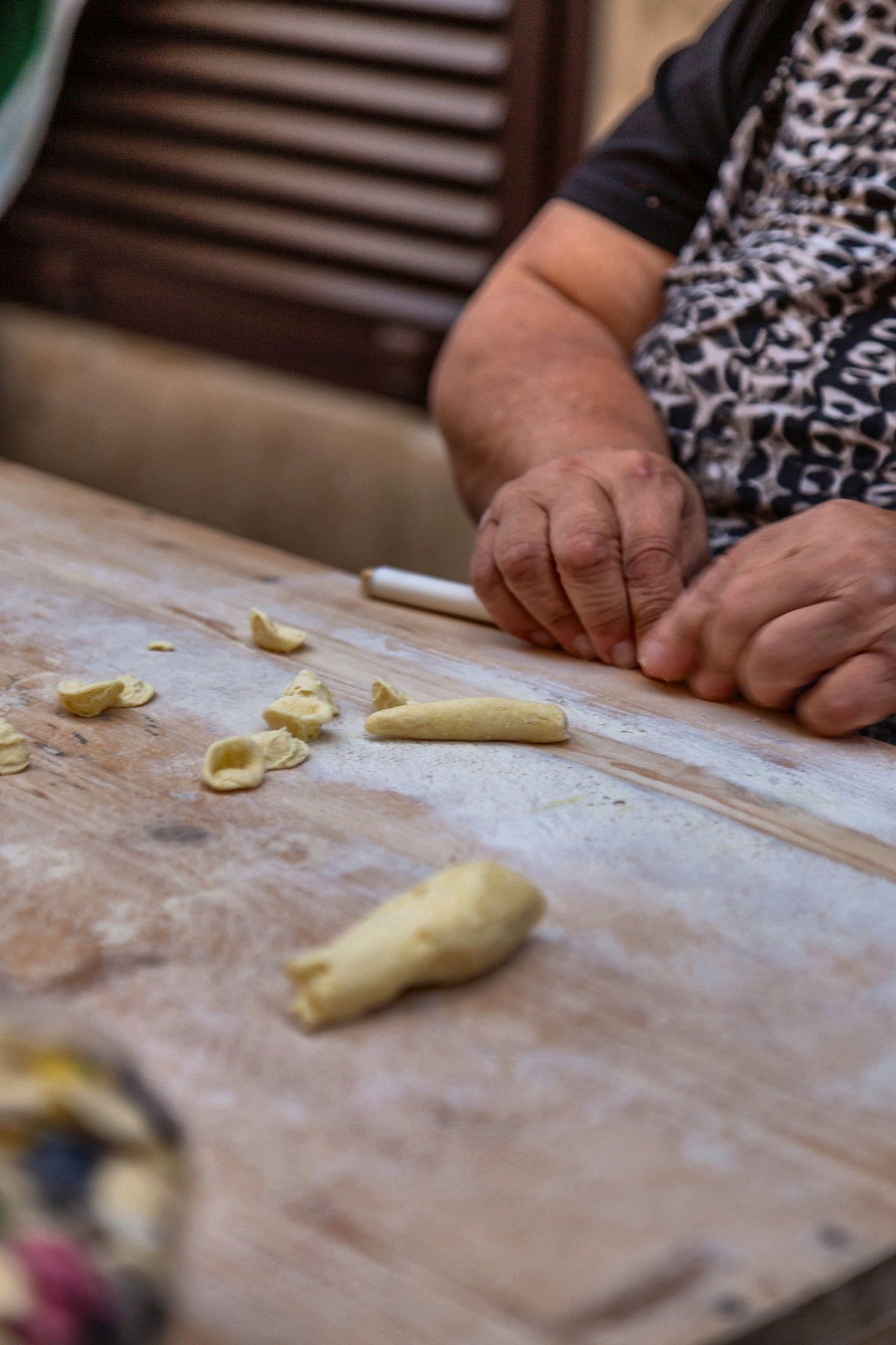 Hands shaping orecchiette with a knife on a wooden board