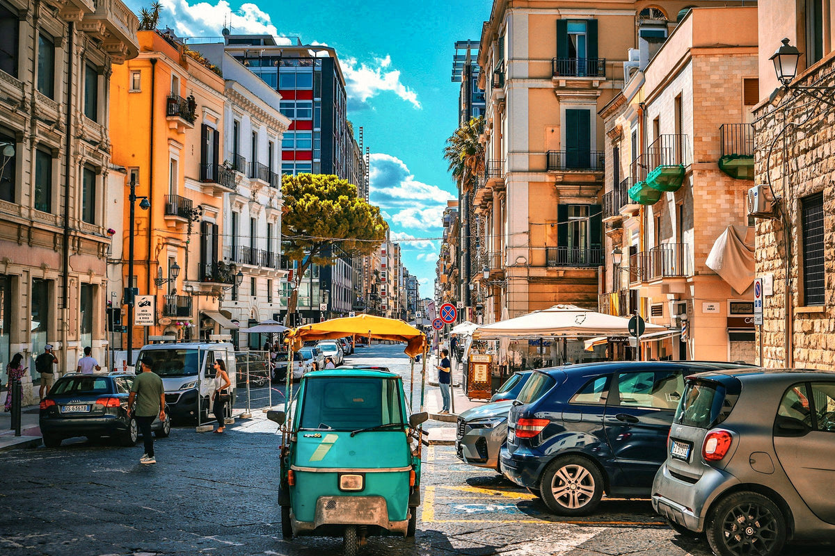 A sunny Bari street with an Ape van, scooters and cafe awnings
