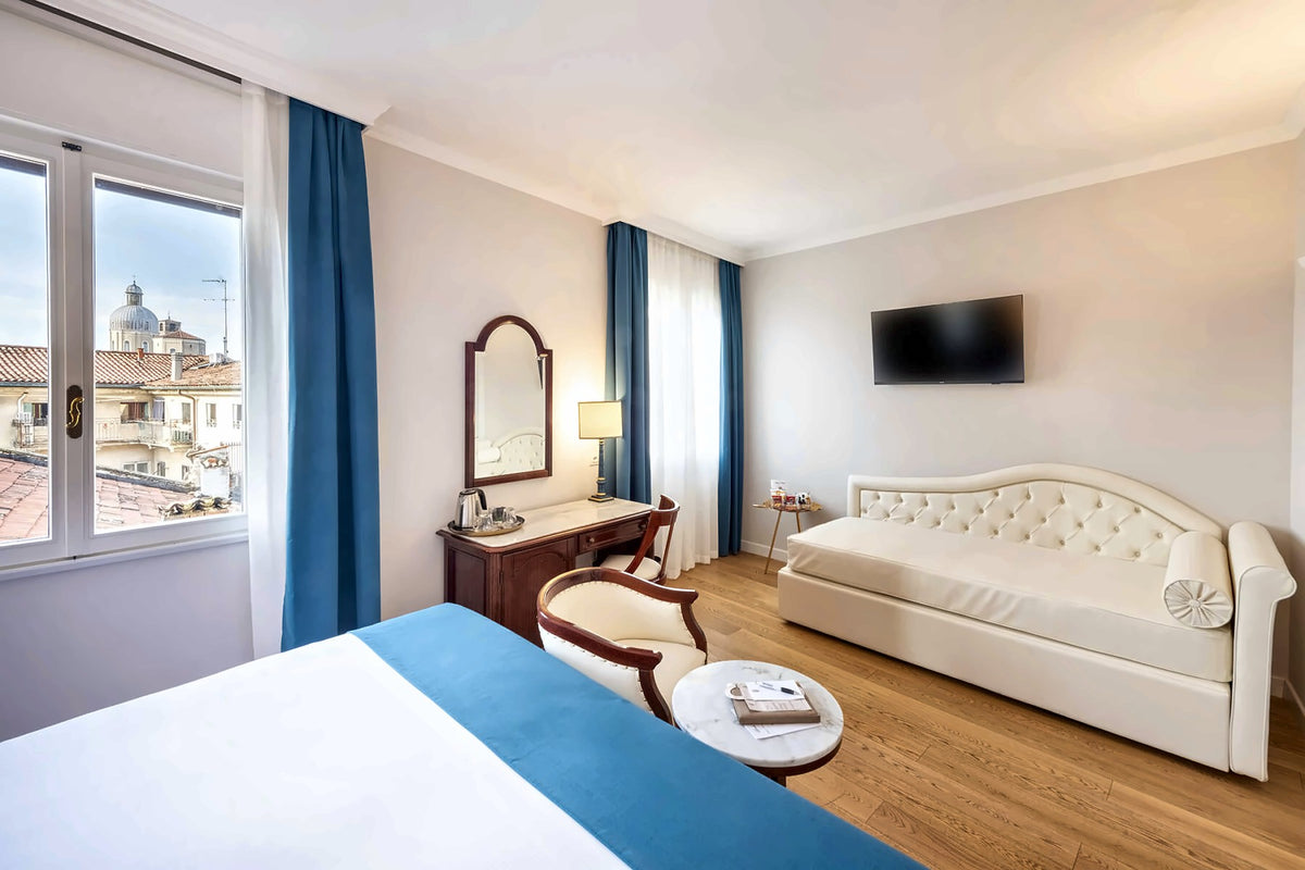 Room at Hotel Majestic Toscanelli with a tufted sofa and a window over Padua rooftops