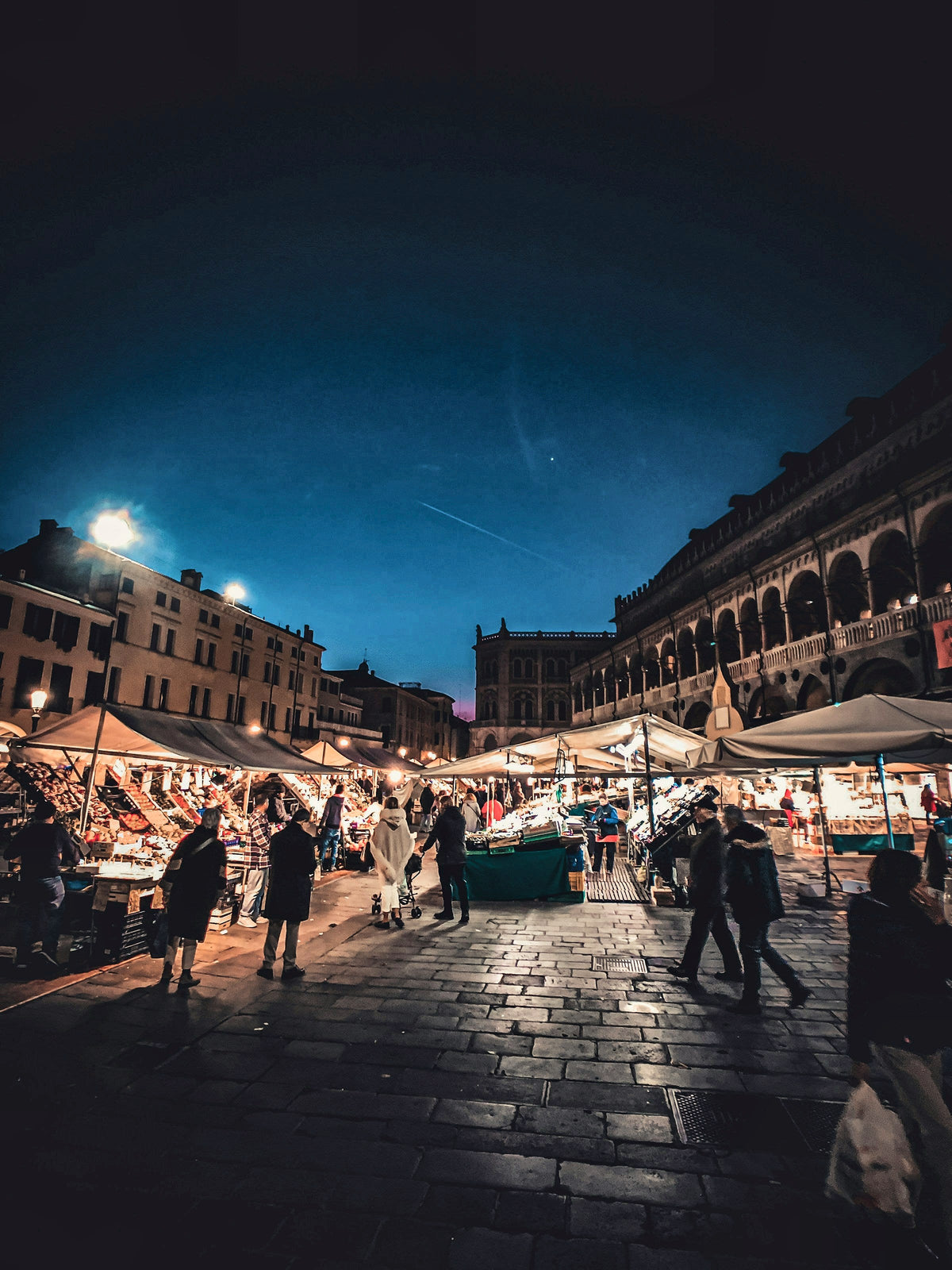 Market stalls lit up beside the Palazzo della Ragione at night