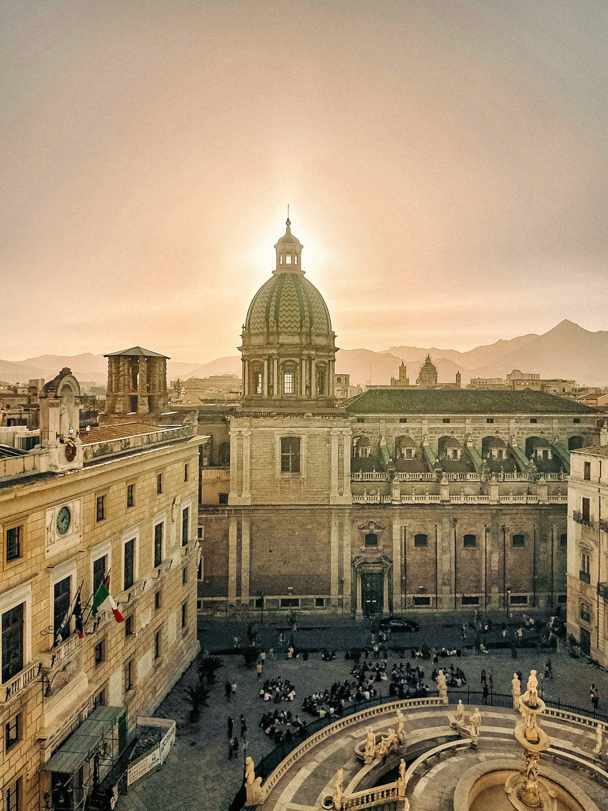 The sun setting behind a Baroque dome above Piazza Pretoria and its fountain