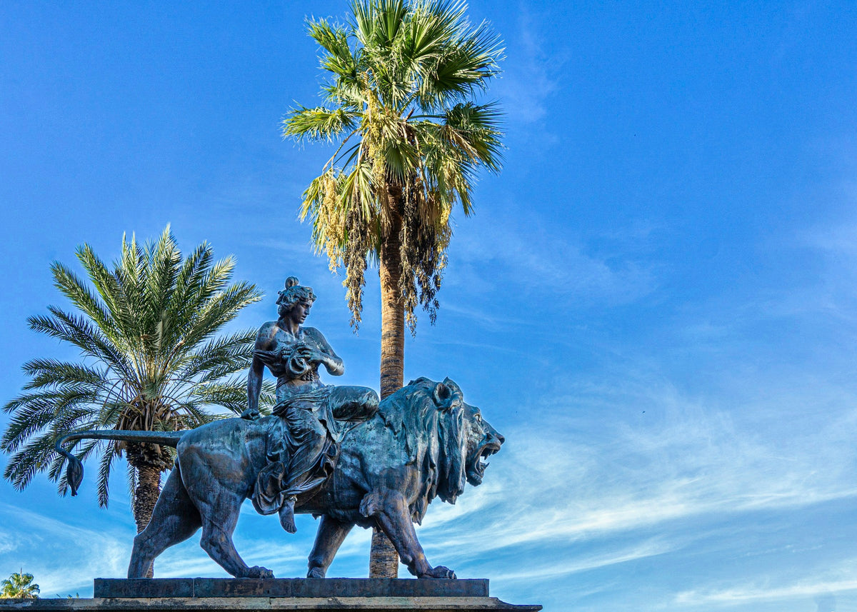 A bronze lion sculpture between the palms outside Teatro Massimo