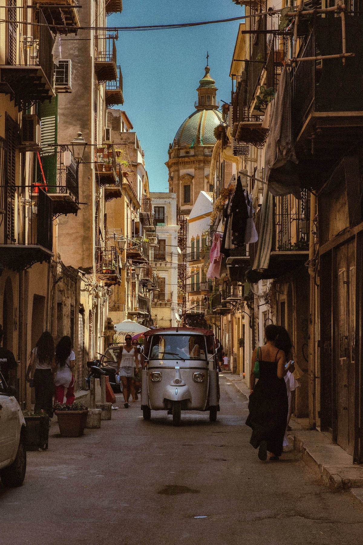 An Ape van and passers-by in a lane below a Baroque dome