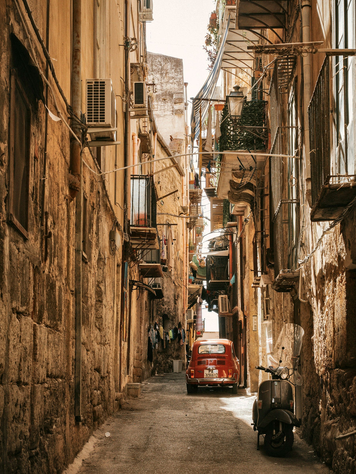 A scooter and a red car in a narrow lane of ochre walls