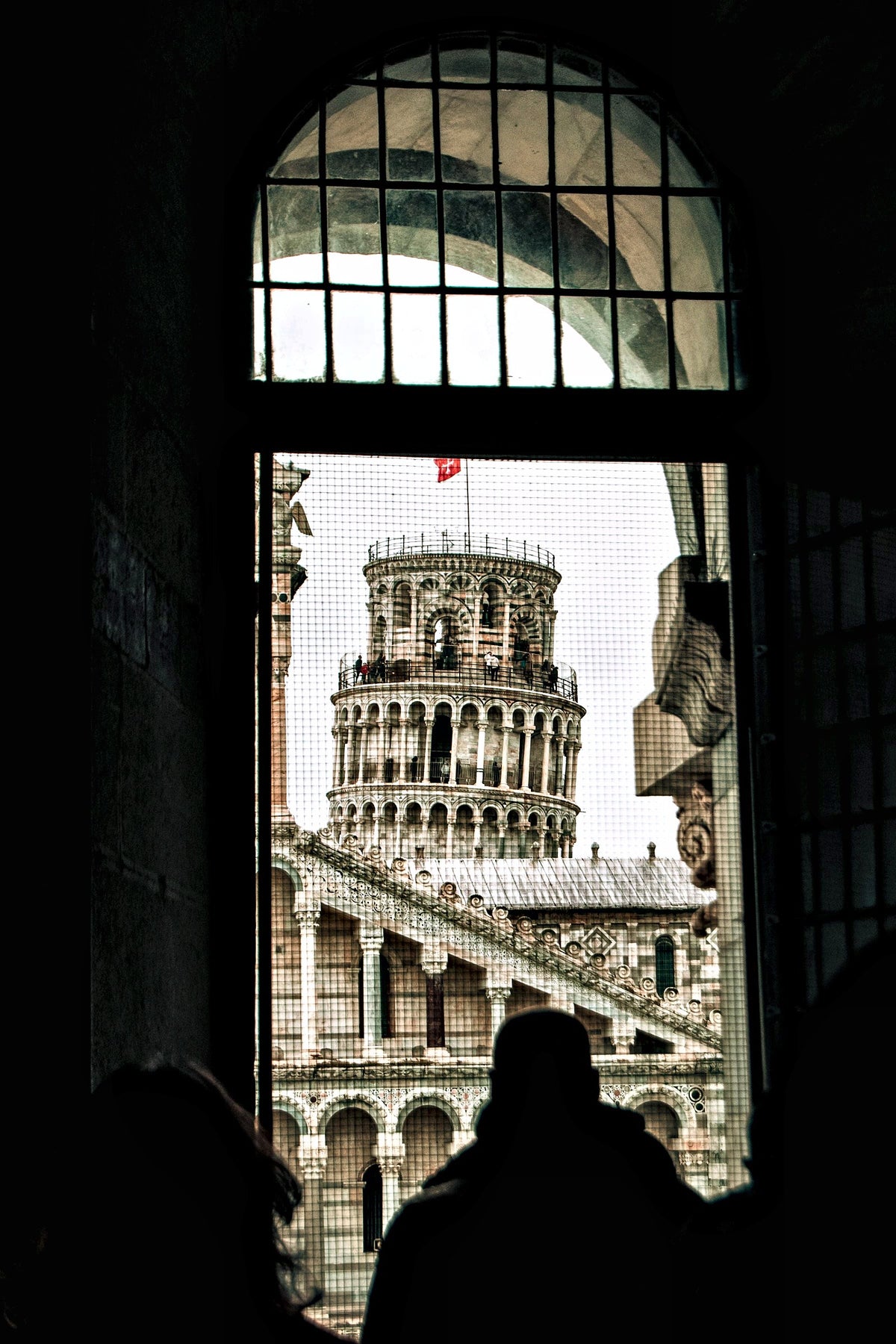 Visitors silhouetted at a window framing the leaning tower