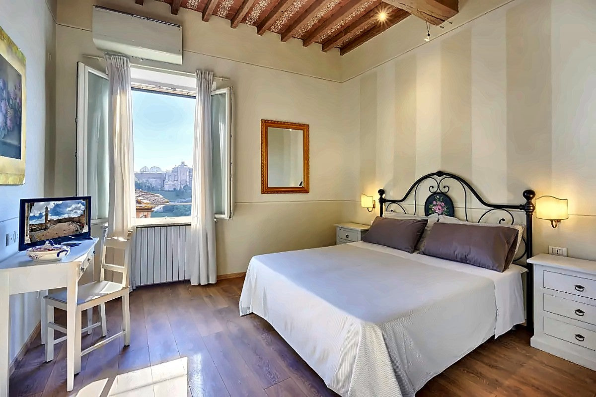 Double room with a wrought-iron bed and a window over the rooftops at I Merli di Ada