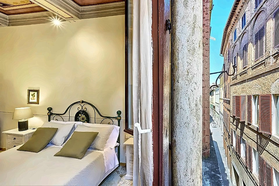 Room with a tall window onto a medieval street at I Merli di Ada