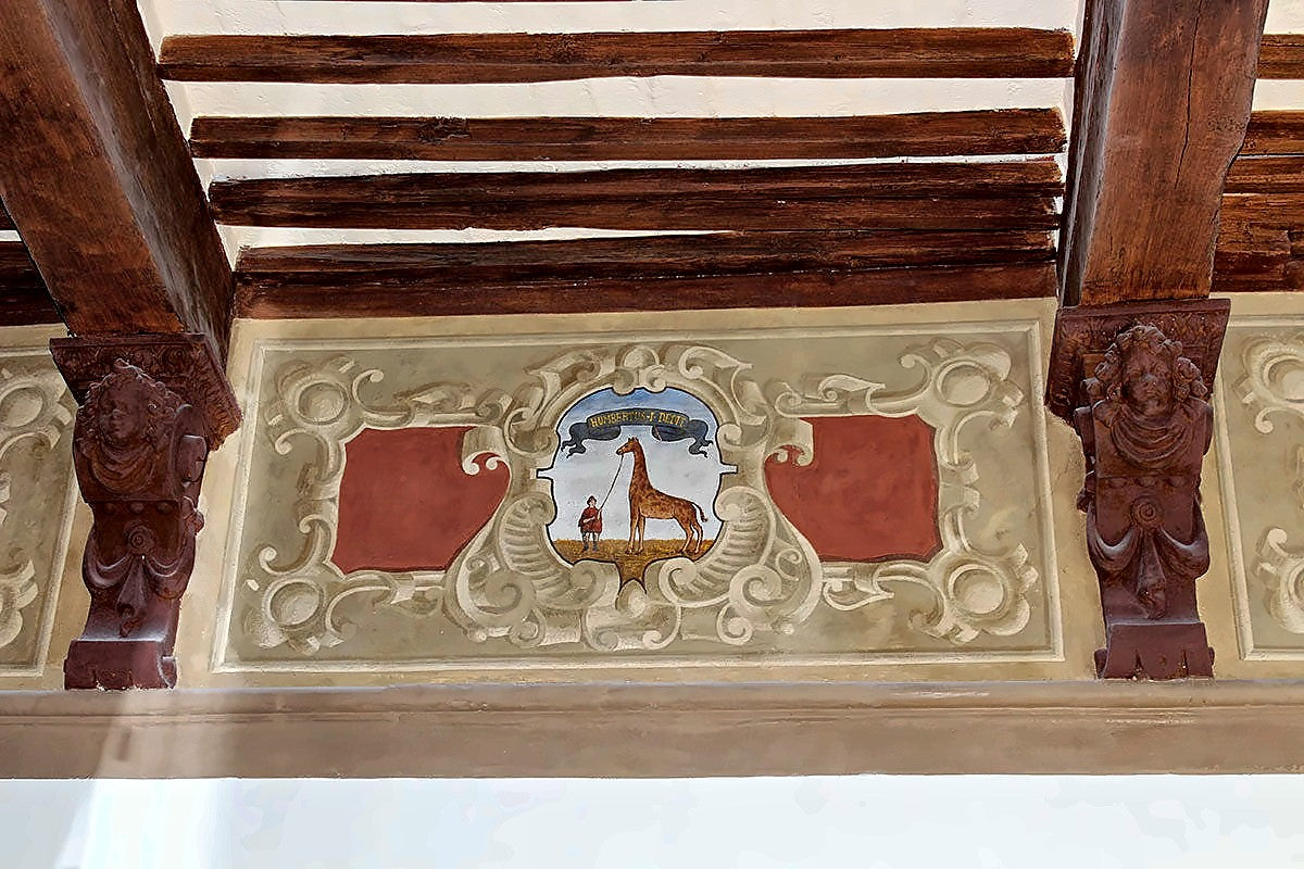 Painted frieze with a coat of arms beneath a wooden ceiling at Hotel Palazzetto Rosso