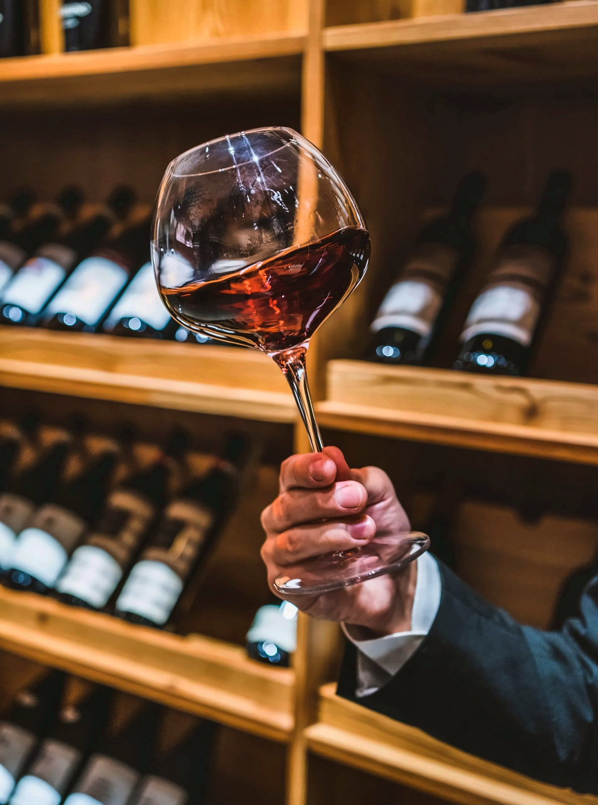 A glass of red wine raised in the cellar at Augurio
