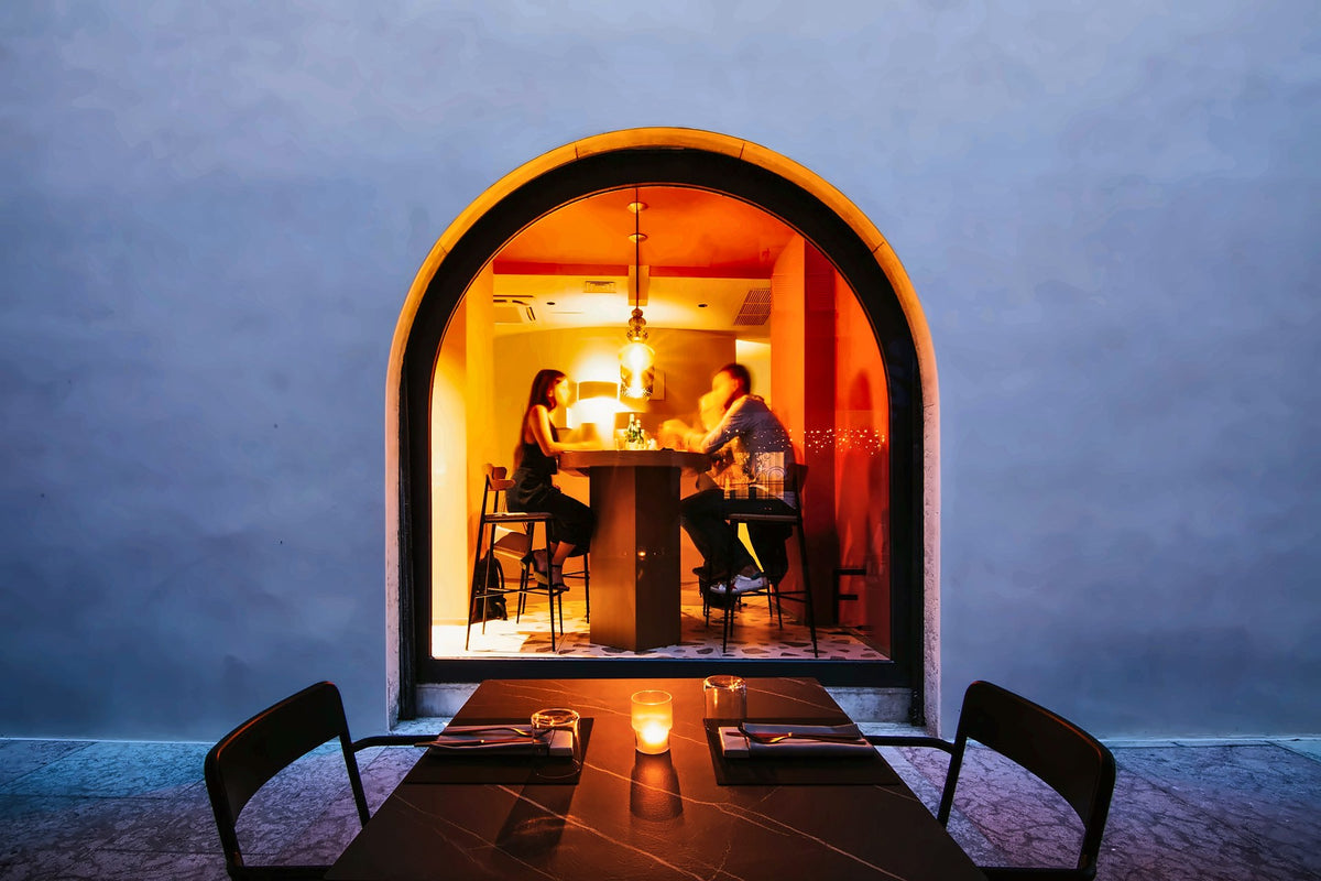 The arched window of La Maison de Filip glowing at dusk