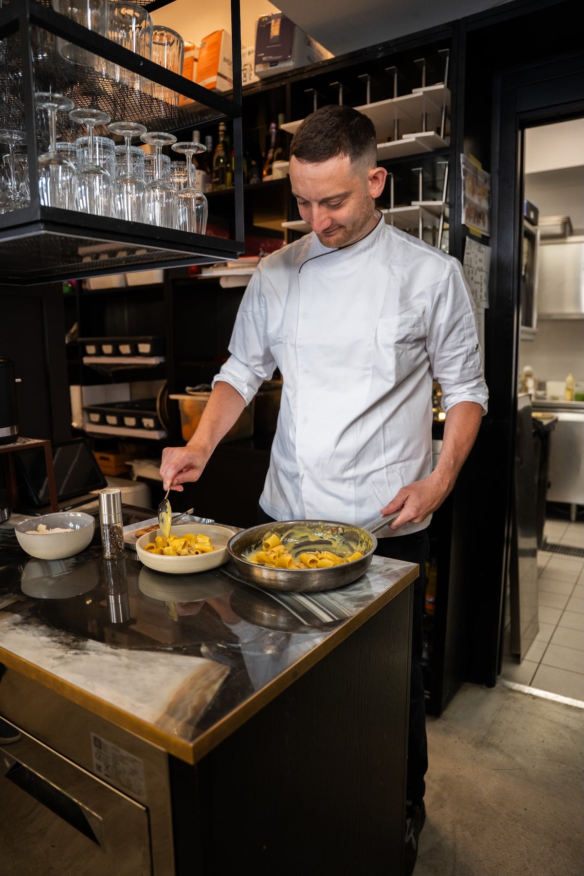 A chef plating pasta in the kitchen at Bottega Comacini