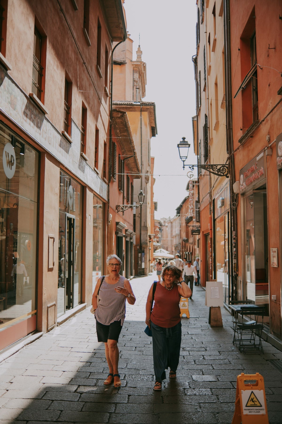 Two elderly women walking down a sunlit narrow street