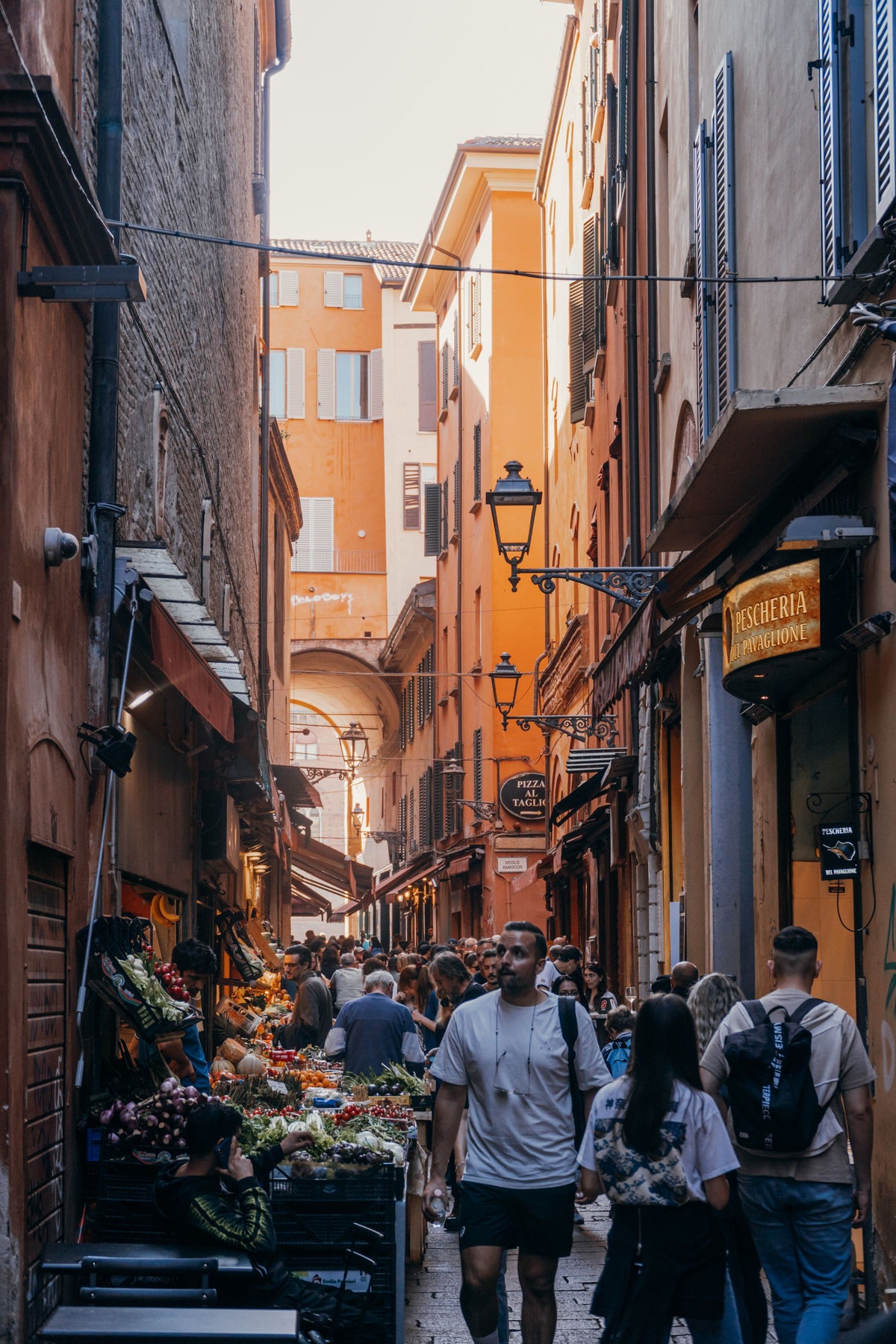 A bustling market alley in Bologna's historic centre, crowded with people