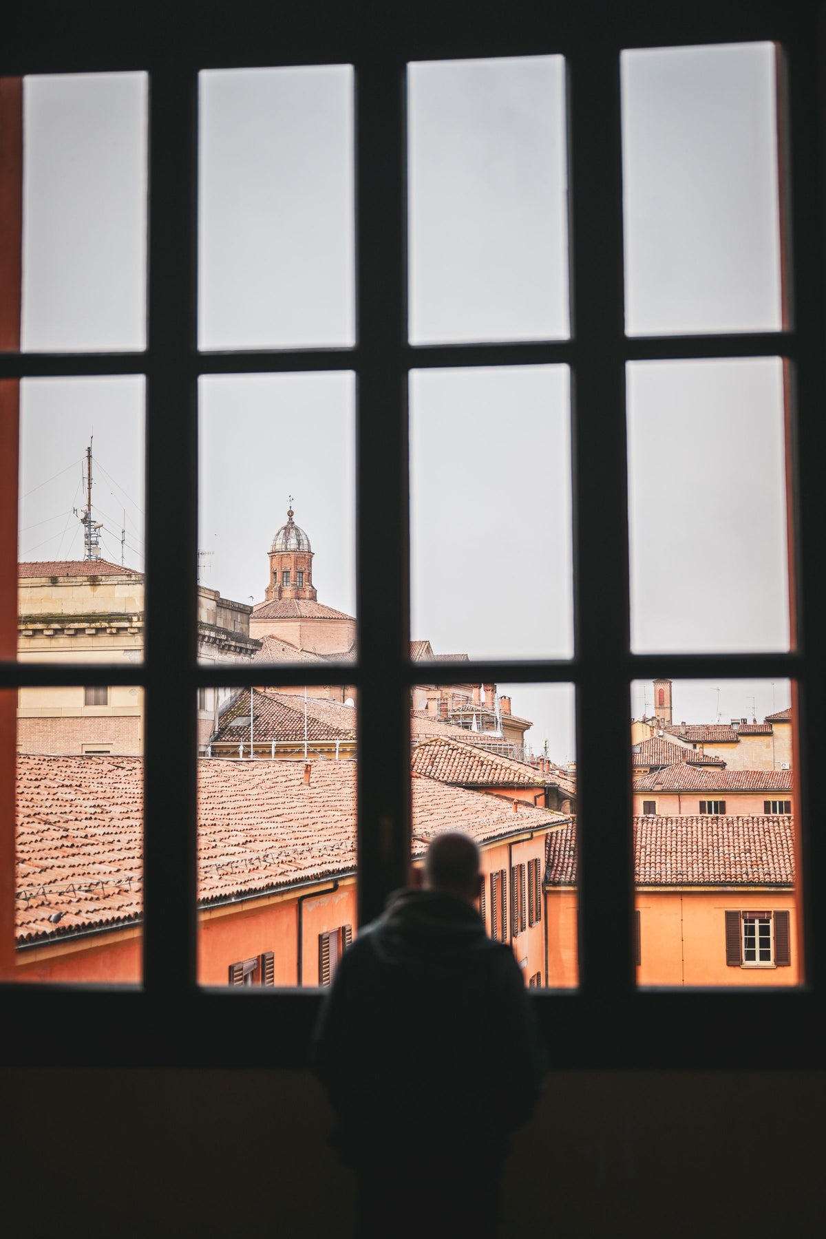 The silhouette of a person looking out at Bologna's historic buildings through a window