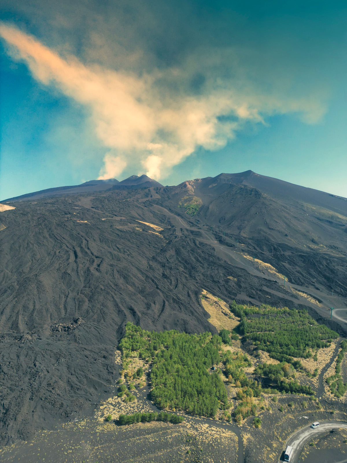 Black lava fields beneath Etna's smoking summit