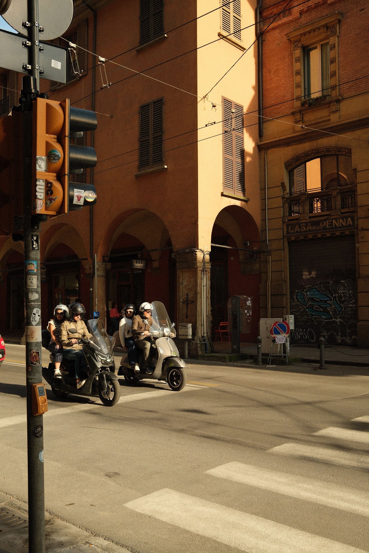 Scooter riders crossing a sunlit street