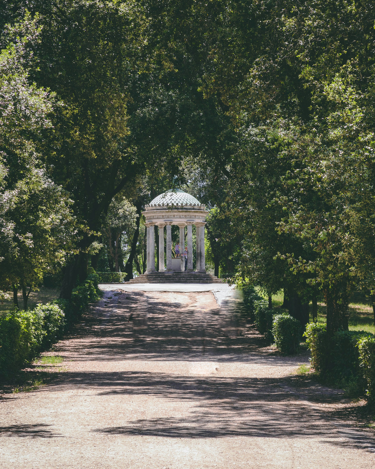 A tree-lined avenue leading to a small temple in Villa Borghese
